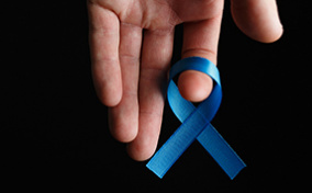 An upside down hand holds a blue ribbon on its index finger.