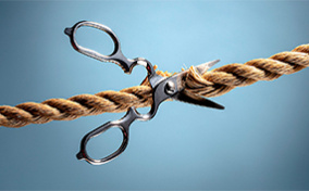 A pair of scissors is cutting a thick brown rope.