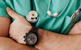 The upper body of a doctor is shown with his arms crossed against his chest.