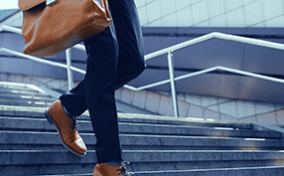 A person walks down the stairs outside while holding a briefcase.