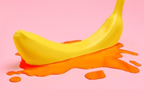 A banana sits in a small pool of blood on a pink background.