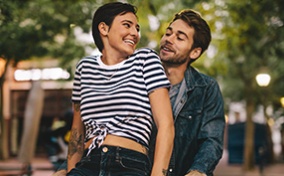 A woman sitting on bicycle handlebars smiles back at the man riding the bike.