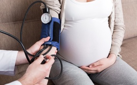 A pregnant woman holds her belly while having her blood pressure tested by a doctor.