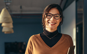 A middle-aged woman holding a tablet smiles into the camera.