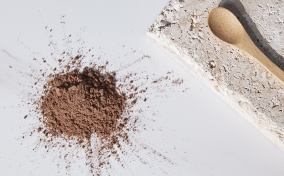 A wooden spoon on a stone plate lies next to a pile of brown powder.