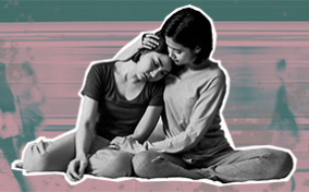 Two women are sitting down and looking sad as one holds the other.