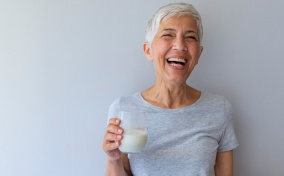 A woman with short white hair holds a glass of milk and laughs.