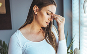 A pregnant woman with a migraine holds her belly and pinches her nose between her eyes.