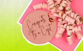 A pink gift sits against a lime green background with a tag that says congrats its a cyst.