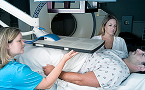 A man with prostate cancer lays under a radiation machine with two technicians next to him.