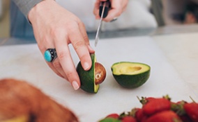 A person cuts an avocado on a cutting board.