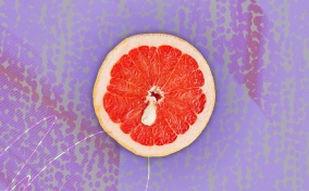Half of a grapefruit is against a purple background and has a white cyst towards the middle of it.
