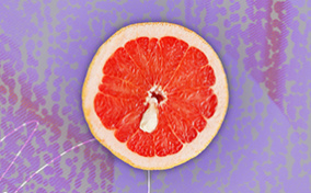 Half of a grapefruit is against a purple background and has a white cyst towards the middle of it.