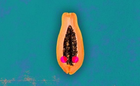 Half of a papaya is against a teal background with two red dots along either side of the open center.