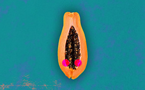 Half of a papaya is against a teal background with two red dots along either side of the open center.