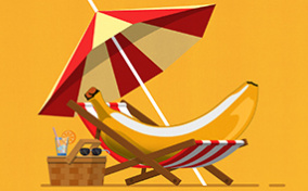 A banana lays in a beach chair underneath an umbrella and next to a picnic basket.