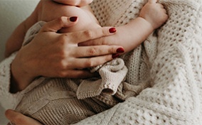 A woman in a knitted sweater holds a baby in her arms.