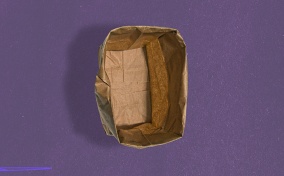 A paper bag stands open with the edges rolled down against a purple background.
