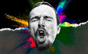 A man makes a face during an orgasm with multiple colors spraying from behind his head.