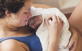 A woman holds her newborn baby after unassisted birth.