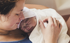 A woman holds her newborn baby after unassisted birth.