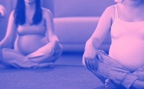 Two pregnant woman sit cross-legged on the floor during childbirth class.