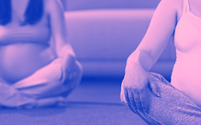 Two pregnant woman sit cross-legged on the floor during childbirth class.