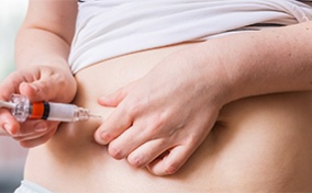 A woman injects fertility hormones inter her hip with a needle.