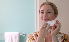 A woman holds a tissue to her face as she cleans it.