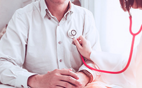 A doctor listens to the heart of a man with her stethoscope.