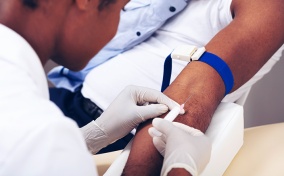 A gloved nurse inserts a needle into a patient's arm.