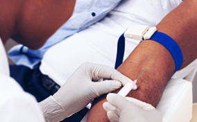 A gloved nurse inserts a needle into a patient's arm.