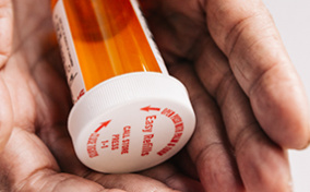 A pair of hands are holding an empty pill bottle.