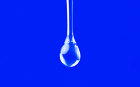 A clear drop of liquid is falling against a bright blue background.