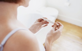 A woman looks down at a pregnancy test in her two hands.