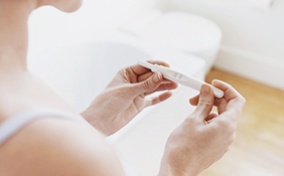 A woman looks down at a pregnancy test in her two hands.