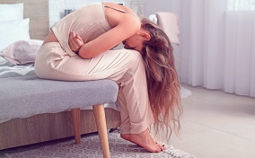 A woman is bent over with her head between her knees while she holds her stomach in pain.