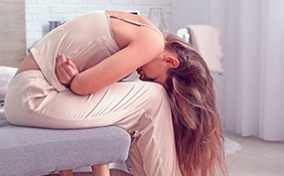 A woman is bent over with her head between her knees while she holds her stomach in pain.