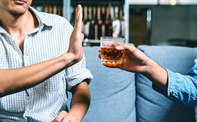 A man holds his hand up to refuse an alcoholic drink being offered to him.