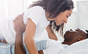 A couple are in bed with a woman on top smiling down at a man.