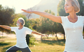 Two seniors do stretches in a field under the sunlight.