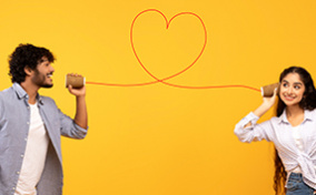 A man talks into a cup with a string in the shape of a heart leading to another cup that has a woman listening.