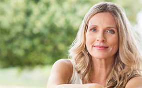A woman sits outside with her arms resting on her knees in a white dress.