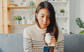 A woman holds up a medicine bottle to her phone on a video call with her telehealth provider.