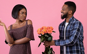 A man tries to give flowers to a woman while she is scowling at him.