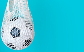 A soccer ball hangs in a white net against a blue background.