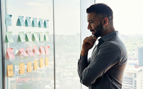 A man stares at a collection of post-it notes placed on a wall at work.