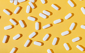 White zinc pills are spread out against a white surface with a pill bottle in the corner.