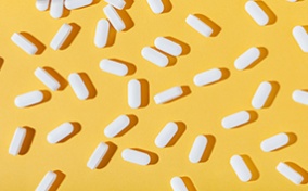 White zinc pills are spread out against a white surface with a pill bottle in the corner.