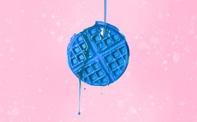 A blue waffle is against a pink background with blue syrup pouring down over it.